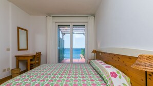 A bedroom with a bed, a desk, a chair, a lamp, and a view of the balcony. - Three-room apartment by Interhome (Monte Argentario)