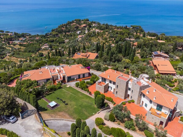 Vista aérea de una zona residencial costera con casas de techo rojo, rodeada de vegetación y una vista despejada del mar.