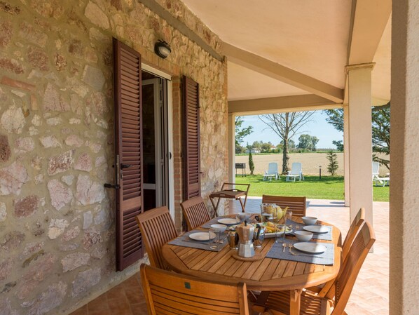 Un comedor al aire libre con paredes de piedra, muebles de madera y vistas al campo.