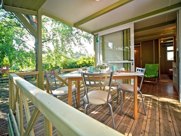 Un área de comedor al aire libre con una terraza de madera, una mesa y sillas, y vistas a la vegetación.