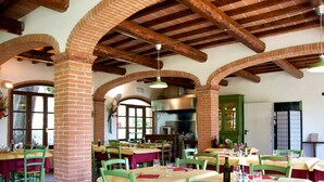Un restaurant avec des arches en briques, des poutres en bois et des chaises vertes. Les tables sont dressées avec des verres à vin et des bouteilles.