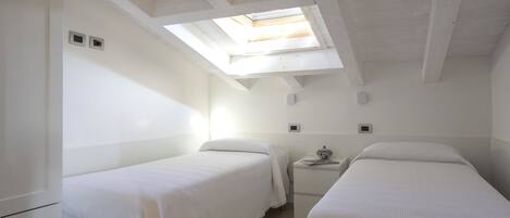 A small, bright room with two beds, a small table, and a skylight.