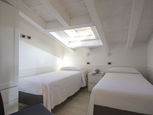 A small, bright room with two beds, a small table, and a skylight.