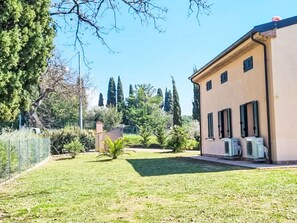 A building with a beige exterior, multiple air conditioning units, and a well-maintained lawn with trees and shrubs.