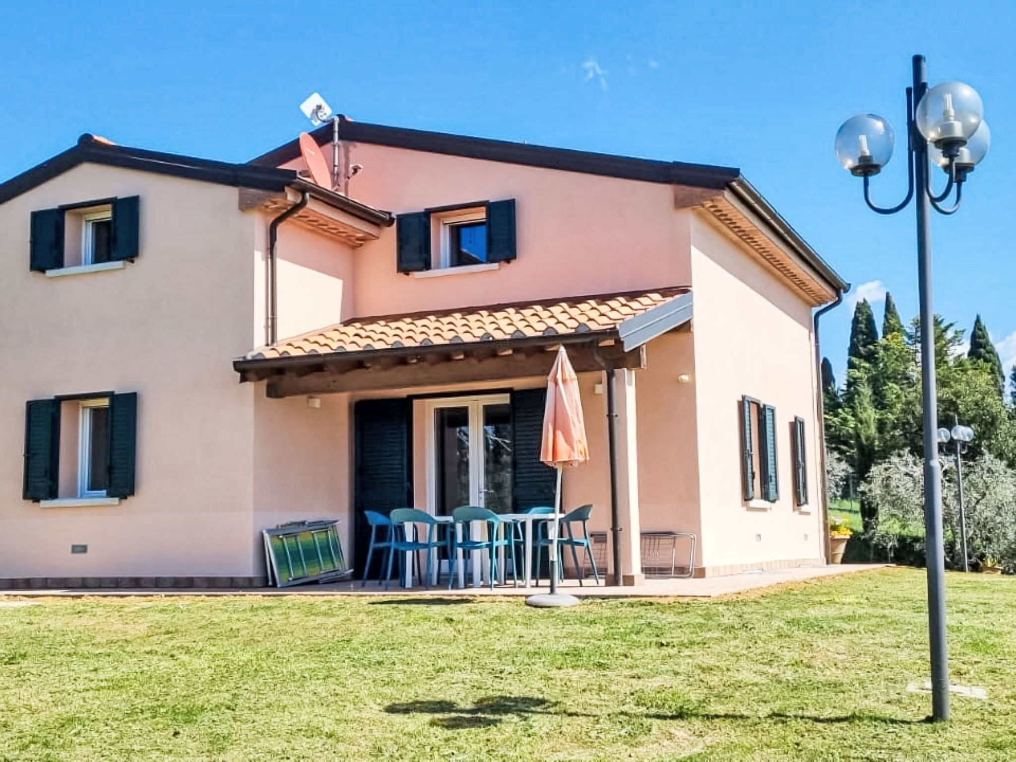 A two-story house with a tiled roof, a covered patio with chairs, and a satellite dish.
