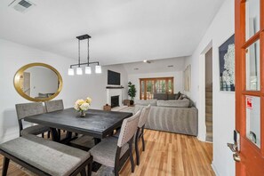 A dining area with a wooden table, chairs, a round mirror, and a hanging light fixture.
