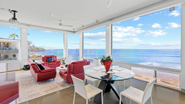 A modern living room with a glass table, red sofas, and a view of the ocean.