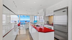 A modern kitchen with a red countertop, stainless steel appliances, and a view of the sea.