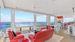 A spacious living area with large windows overlooking the ocean, a red sofa, a coffee table, and a dining area with red and white decor.