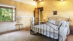 A bedroom with a metal bed frame, a window with a view of greenery, a chair, and a wooden ceiling. - I Limoni (BUT151) by Interhome (Buti)
