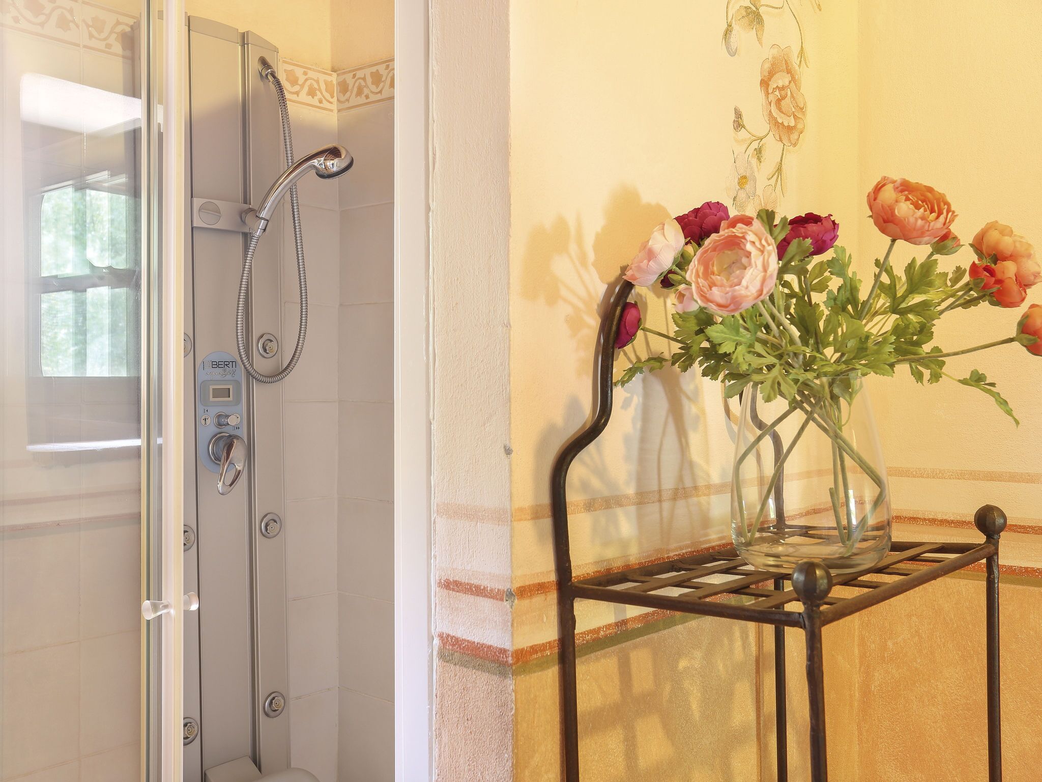 A bathroom with a shower, a toilet, and a vase with flowers on a shelf.