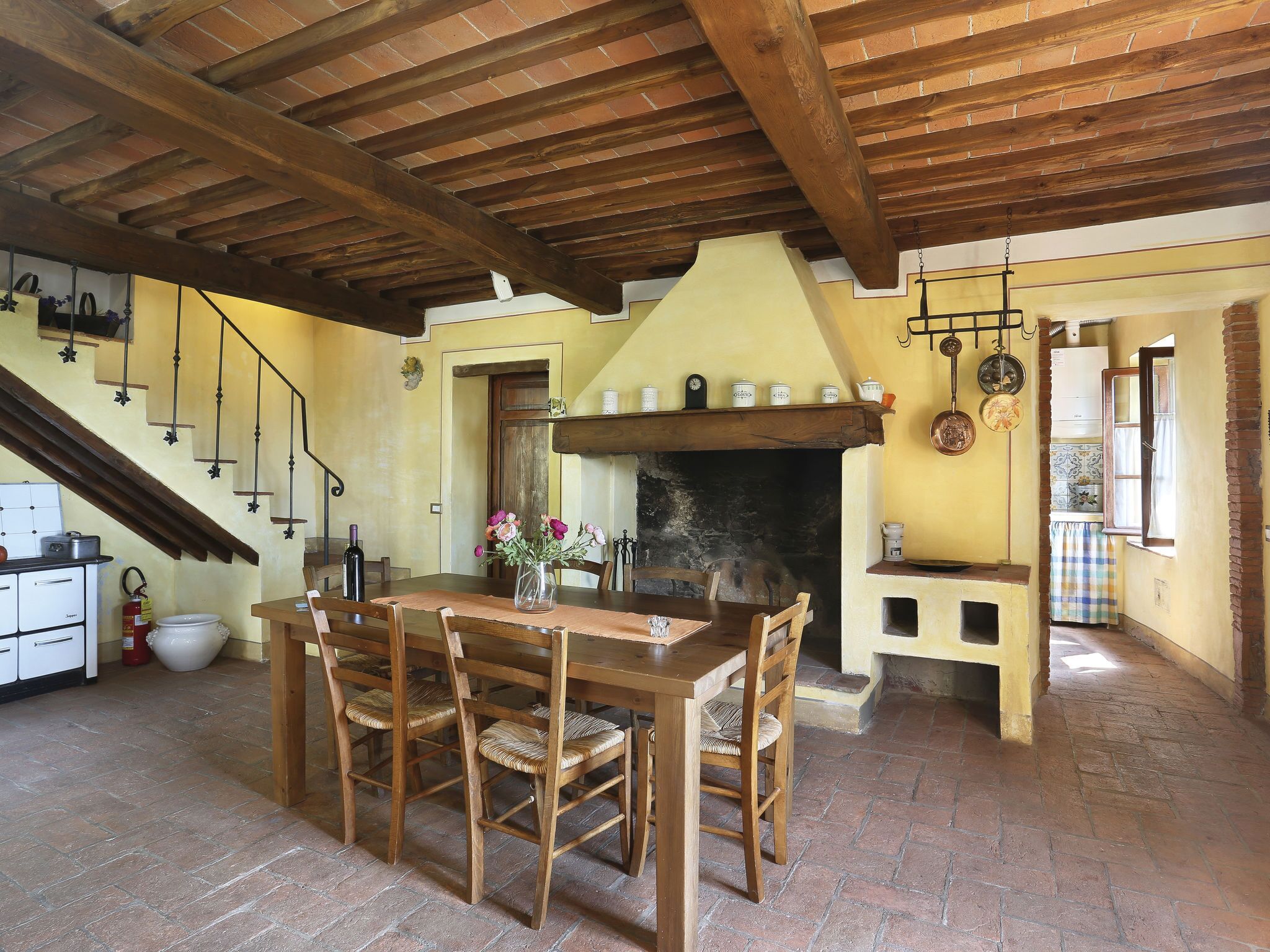 Un'area pranzo rustica con tavolo e sedie in legno, un camino e una cucina sullo sfondo.