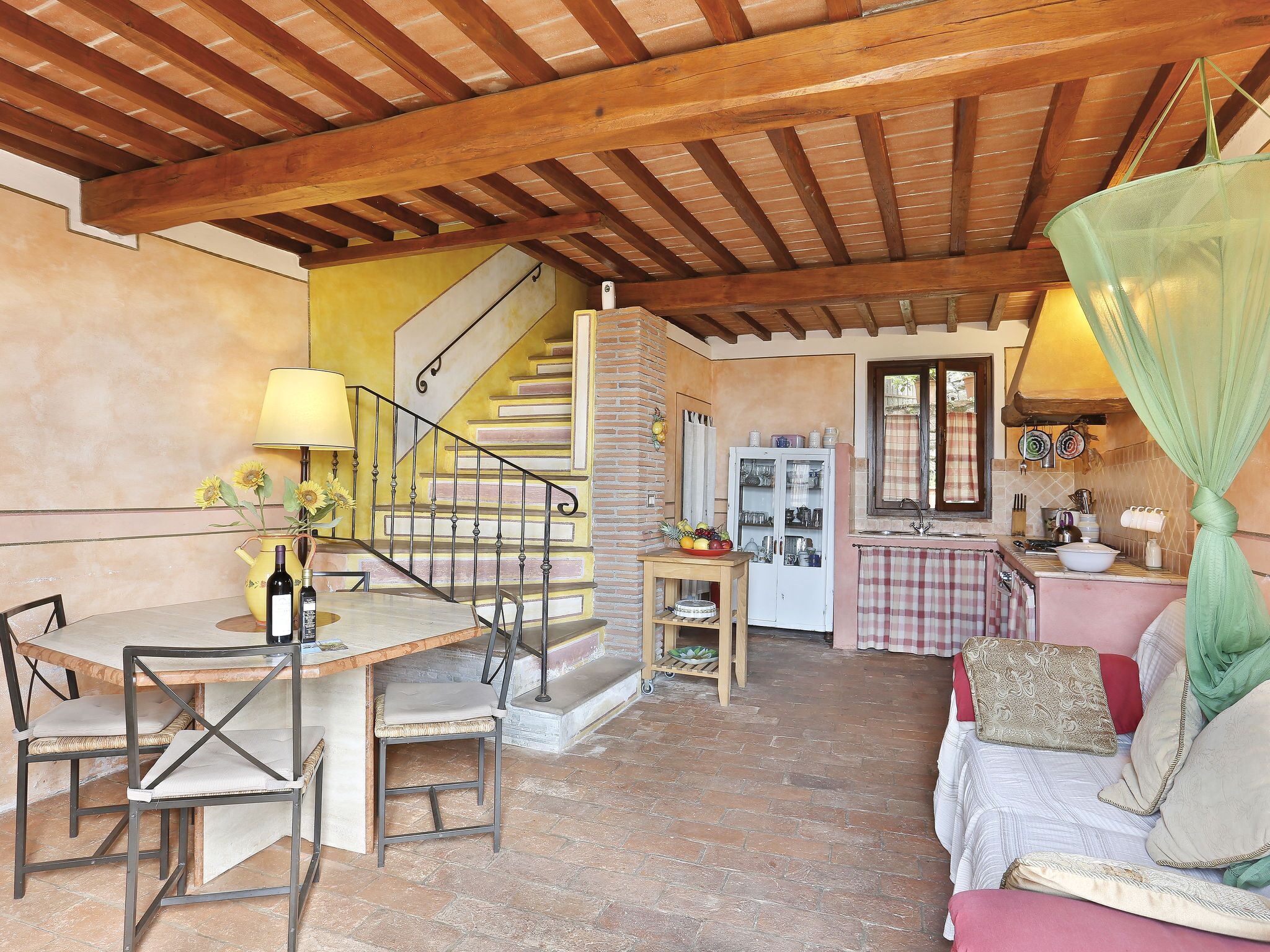 Un intérieur chaleureux avec un plafond en bois, un escalier, un coin repas avec des chaises et une table, et un espace cuisine équipé d’un évier et de placards.