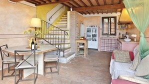 Un intérieur chaleureux avec un plafond en bois, un escalier, un coin repas avec des chaises et une table, et un espace cuisine équipé d’un évier et de placards.