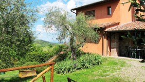Uma casa rústica com base de pedra, telhado de telhas e um jardim com diversas plantas e cerca de madeira.
