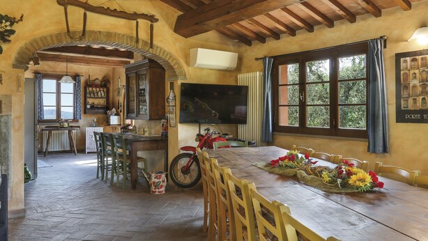 Uma área de jantar rústica com mesa e cadeiras de madeira, uma motocicleta e uma TV fixada na parede.