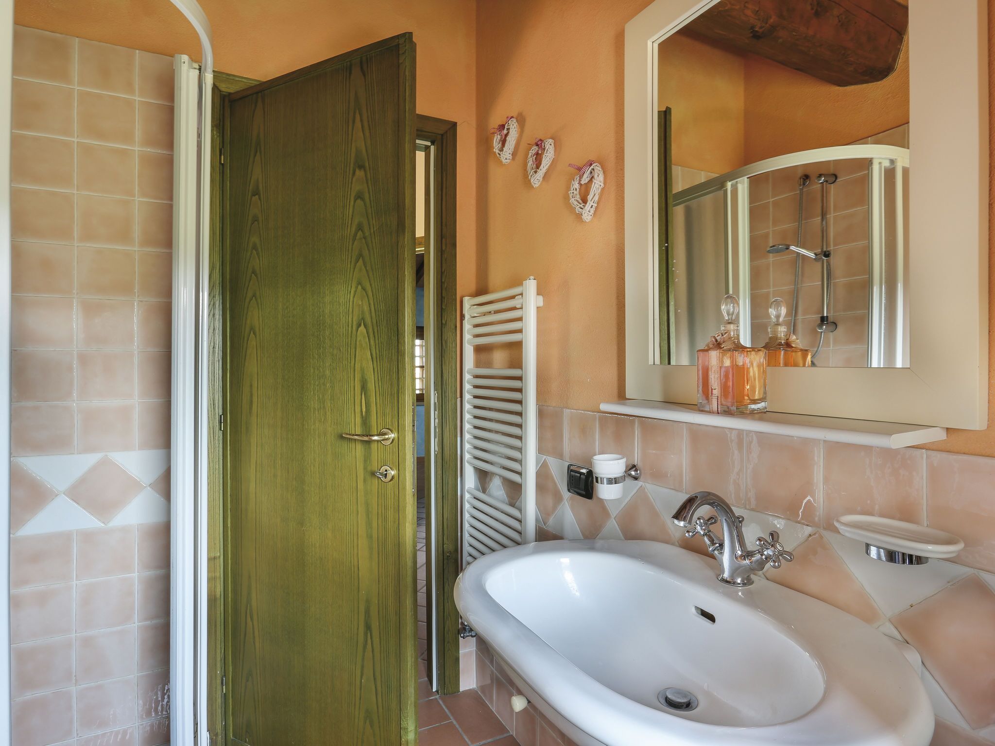 Un baño con puerta de madera, un lavabo blanco, un espejo y zona de ducha.