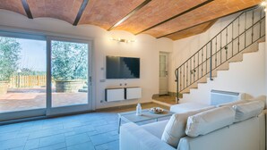 Ein geräumiges Wohnzimmer mit einem weißen Sofa, einem Flachbildfernseher und einer Treppe.