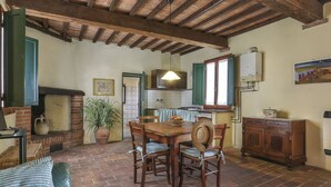 A rustic kitchen with a brick fireplace, wooden ceiling beams, and a dining area with a table and chairs. - Carbonaia (PAA133) by Interhome (Palaia)