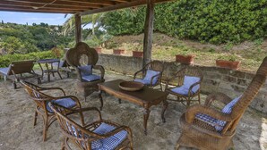 An outdoor patio with wicker furniture and a table, surrounded by a stone wall and lush greenery. - Carbonaia (PAA133) by Interhome (Palaia)