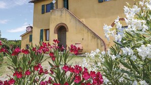 A yellow building with a staircase leading to a door, surrounded by red and white flowers. - Carbonaia (PAA134) by Interhome (Palaia)