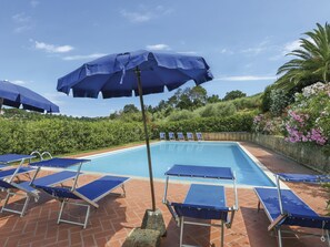 Une piscine entourée de verdure et d’un mur de pierre, avec des chaises longues bleues et des parasols.