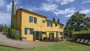 A yellow building with green shutters, a gravel driveway, and a grassy lawn. - Favilli (PAA130) by Interhome (Palaia)