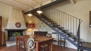 A dining area with a brick floor, wooden table, and chairs, a fireplace with a decorative plate, and a staircase with a metal railing. - Favilli (PAA130) by Interhome (Palaia)