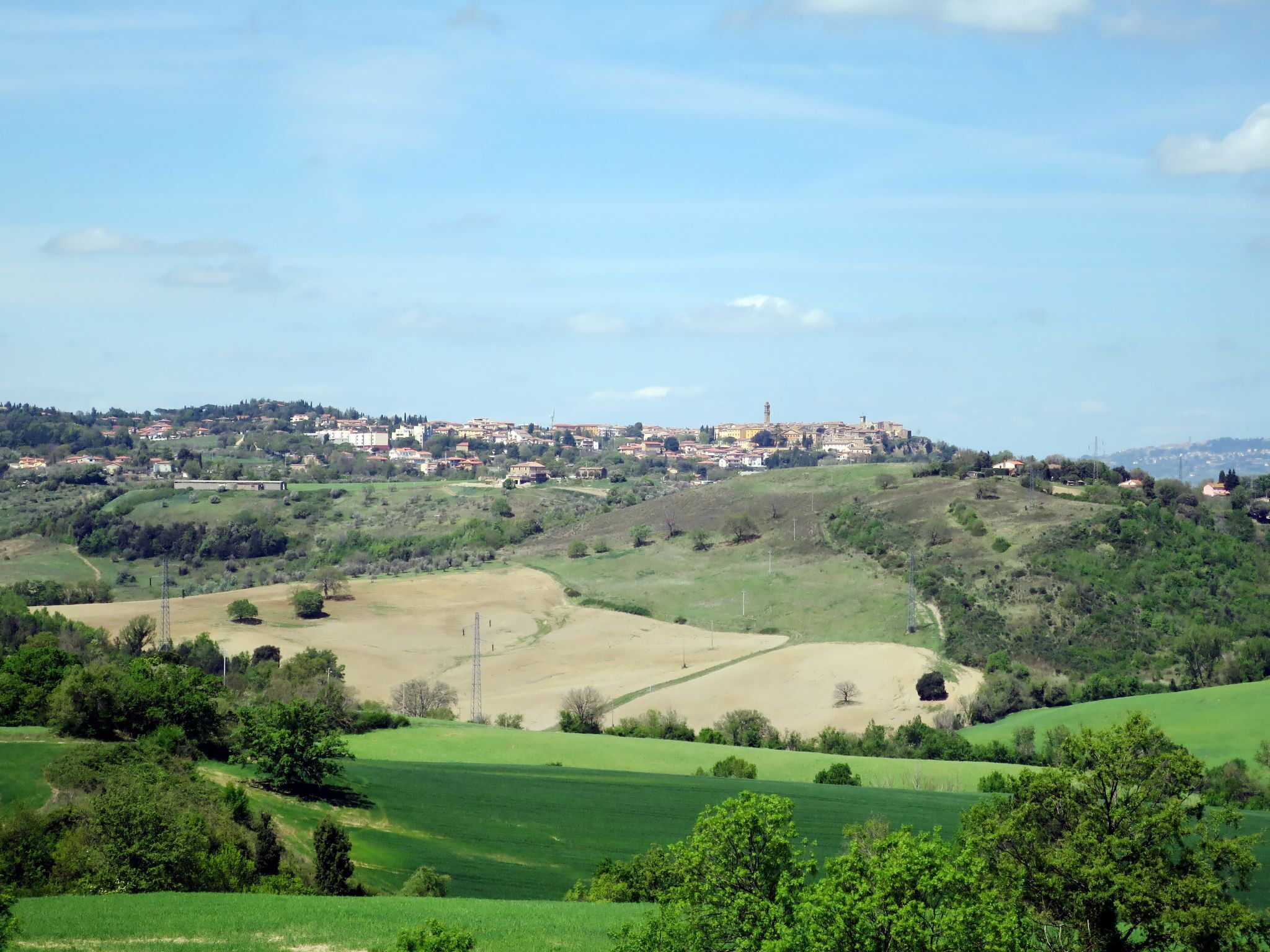 Un paisaje rural con colinas ondulantes, un pueblo pequeño al fondo y una torre destacada.