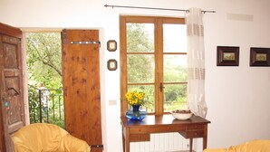 Una habitación con puerta de madera, ventana con vistas a la vegetación, una mesa con tetera y tazas, y dos sillas amarillas.