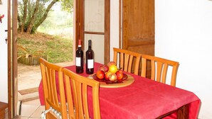 Un comedor con mantel rojo, sillas de madera y un cuenco de frutas. Hay dos botellas de vino sobre la mesa.