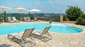 Un espace piscine agrémenté de chaises longues et de parasols, entouré de dalles de pierre et offrant une vue sur la campagne.
