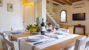 Un coin repas avec une table dressée pour deux personnes, agrémenté d’une bouteille de vin, de verres et d’une présentation de fruits.