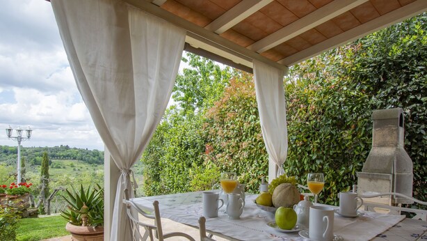Un espace extérieur abrité, aménagé pour prendre les repas, avec une table dressée pour le petit-déjeuner, entouré d’une végétation luxuriante et offrant une vue pittoresque.