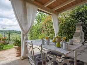 Un espacio de comedor al aire libre con techo, con una mesa preparada para el desayuno, rodeado de abundante vegetación y una vista panorámica.