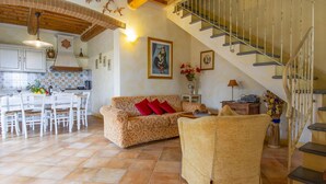 Un vaste espace de vie comprenant un canapé, une table à manger avec des chaises, un escalier et une cuisine en arrière-plan.