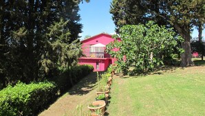 Un bâtiment rose doté d’un patio couvert, entouré d’arbres et d’une pelouse.