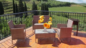 Une terrasse meublée de mobilier en osier et agrémentée d’un vase de tournesols, d’où l’on peut admirer un paysage verdoyant, avec des arbres et des champs.