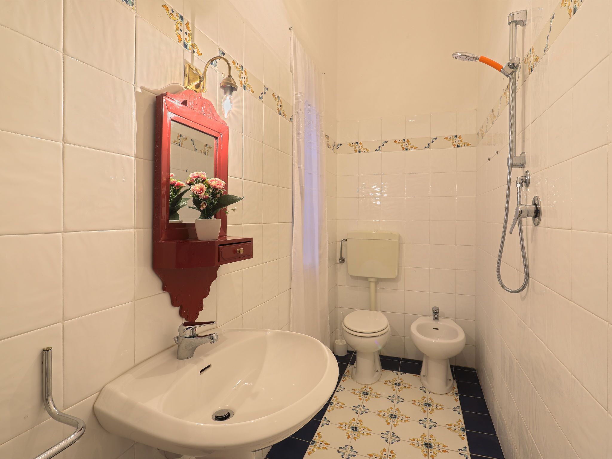 Et badeværelse med en hvid vask, et spejl med rød ramme, et toilet og en bidet.