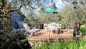 A patio with white plastic chairs and a table, surrounded by a metal fence, with a stone wall and greenery in the background. - Conte Francesco II by Interhome (Certaldo)