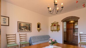 Comedor con mesa de madera, sillas, banco, candelabro, estanterías en la pared y un cuadro.