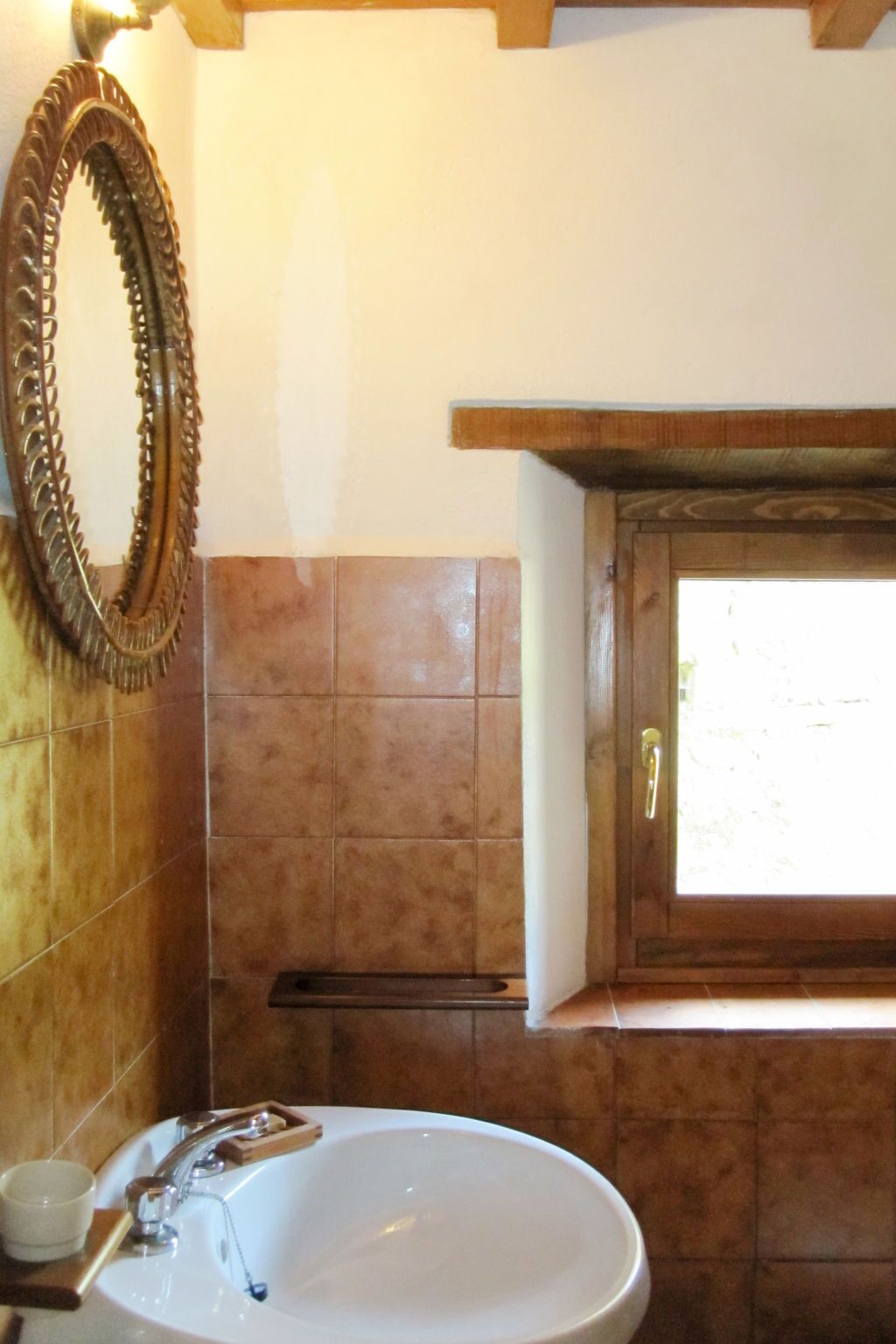 Ein Badezimmer mit einem weißen Waschbecken, einem Spiegel und einem Fenster über dem Waschbecken.