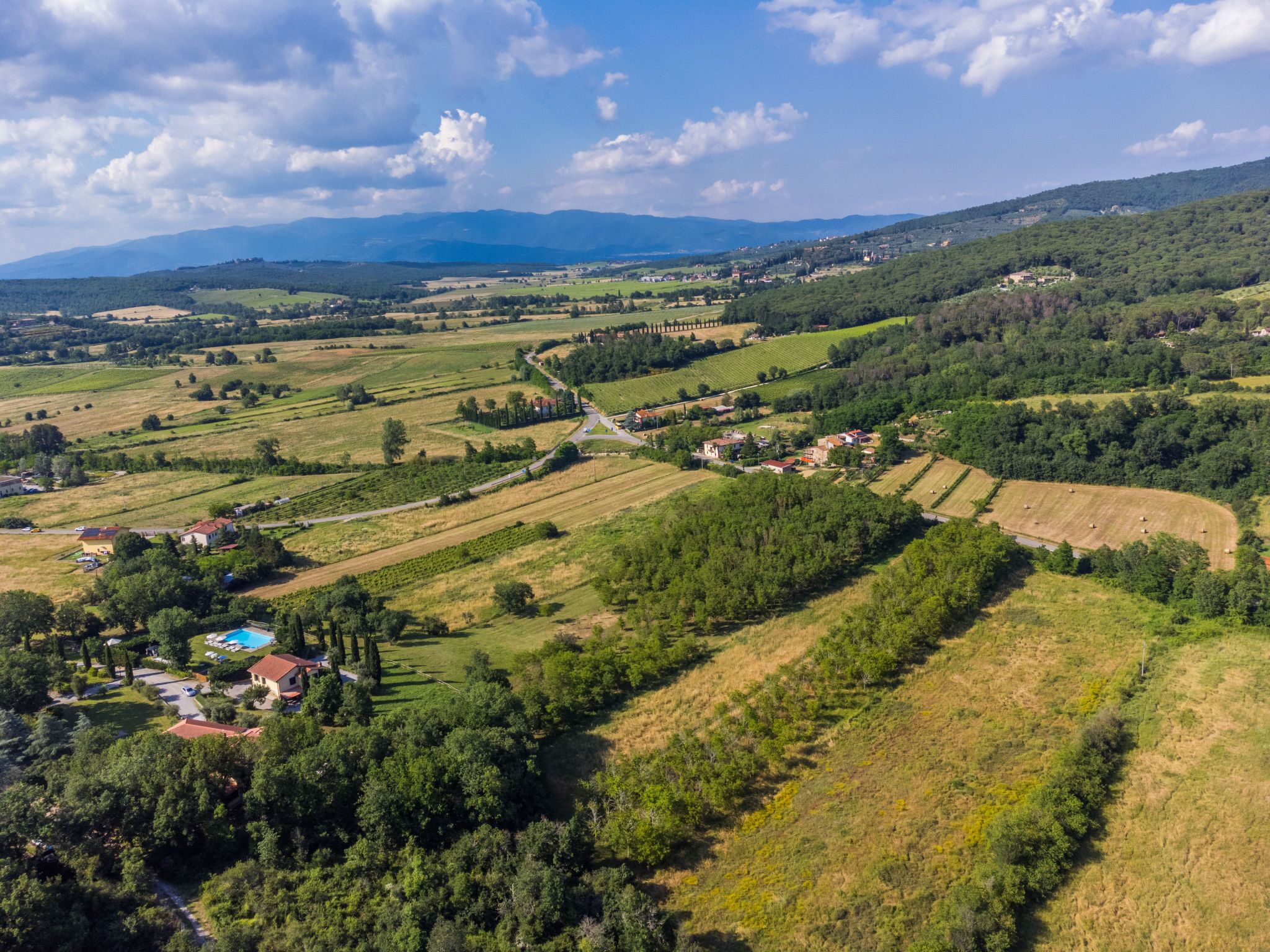 An aerial view of a rural landscape with fields, a winding road, and scattered buildings.