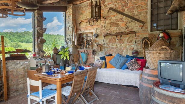 Un interior rústico con pared de piedra, mobiliario de madera y vista al campo.