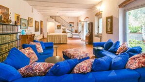 Een ruime woonkamer met een blauwe zithoek, een trap naar een eetgedeelte, en een groot raam met uitzicht op het groen.