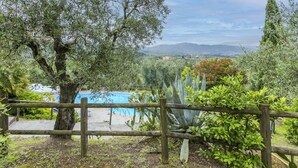 A pool area with a wooden fence, surrounded by olive trees and various plants, overlooking a scenic landscape with mountains in the distance. - San Lazzaro by Interhome (Monsummano Terme)