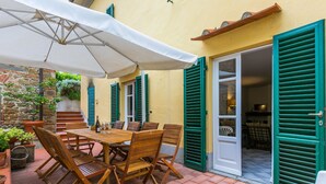 An outdoor patio with a wooden table and chairs, a white umbrella, and green shutters on the building. - San Lazzaro by Interhome (Monsummano Terme)