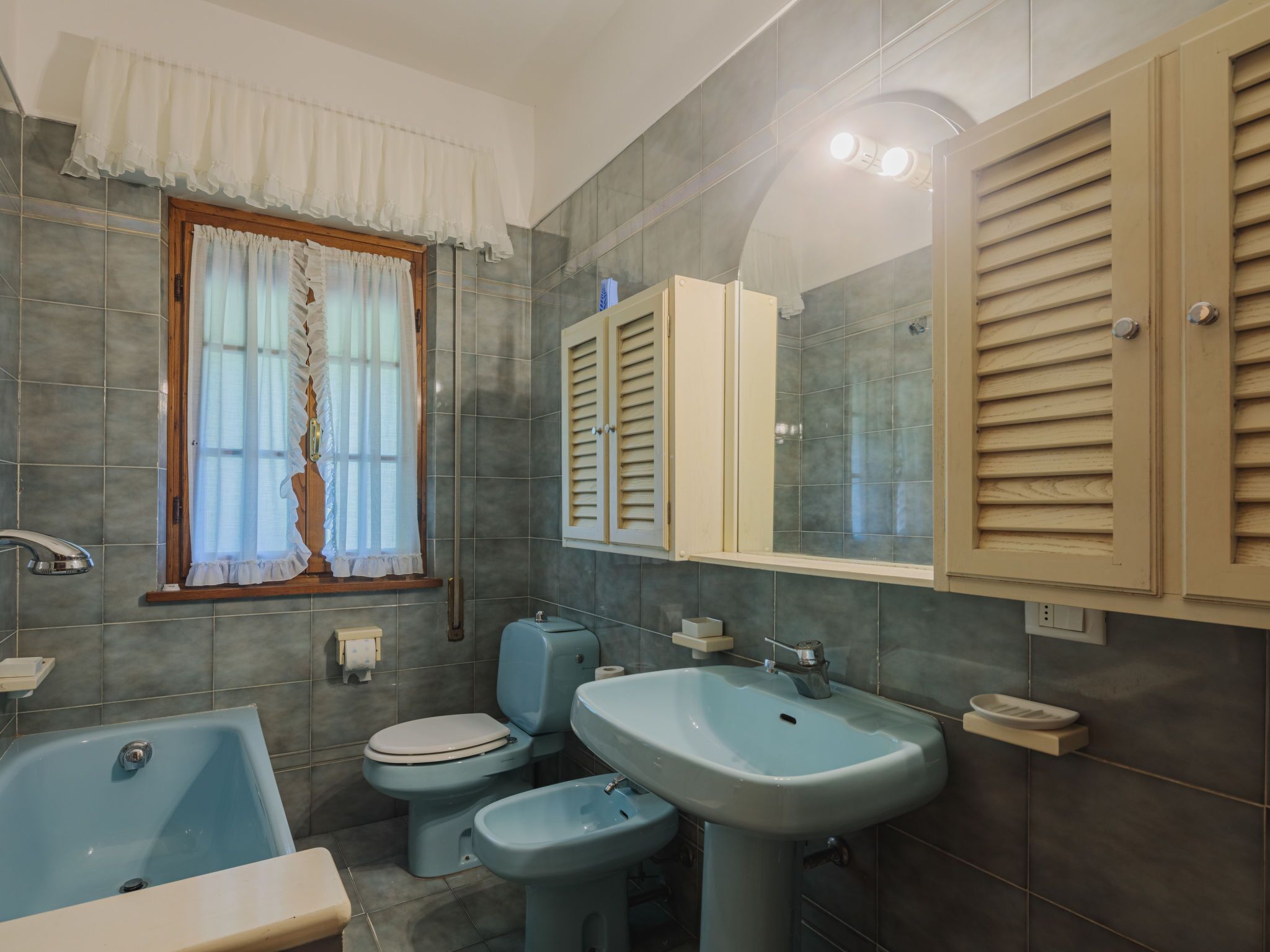 Une salle de bain avec une baignoire, deux lavabos, des toilettes et une fenêtre avec des rideaux.