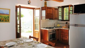 A dining area with a table set for four, a kitchen with wooden cabinets, a stove, and a refrigerator. - L'Uccelliera by Interhome (San Giuliano Terme)