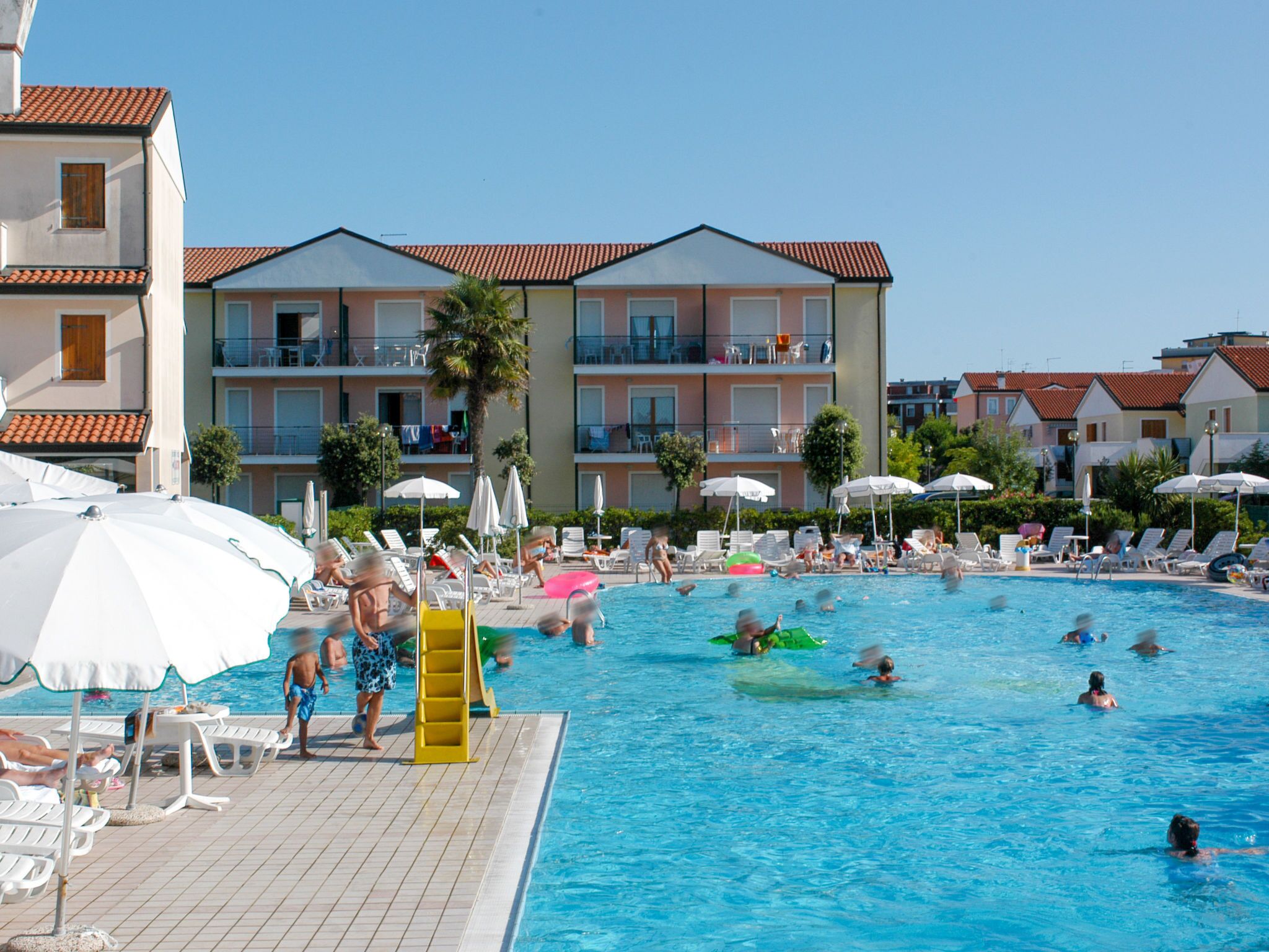 A swimming pool area with lounge chairs and umbrellas, surrounded by multi-story buildings with balconies.